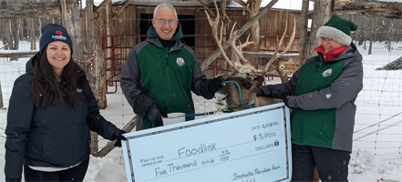 Two people with a reindeer presenting a large check to a charity worker.